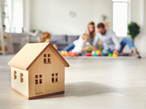 makieta drewnianego domku na podłodze, w tle rodzina